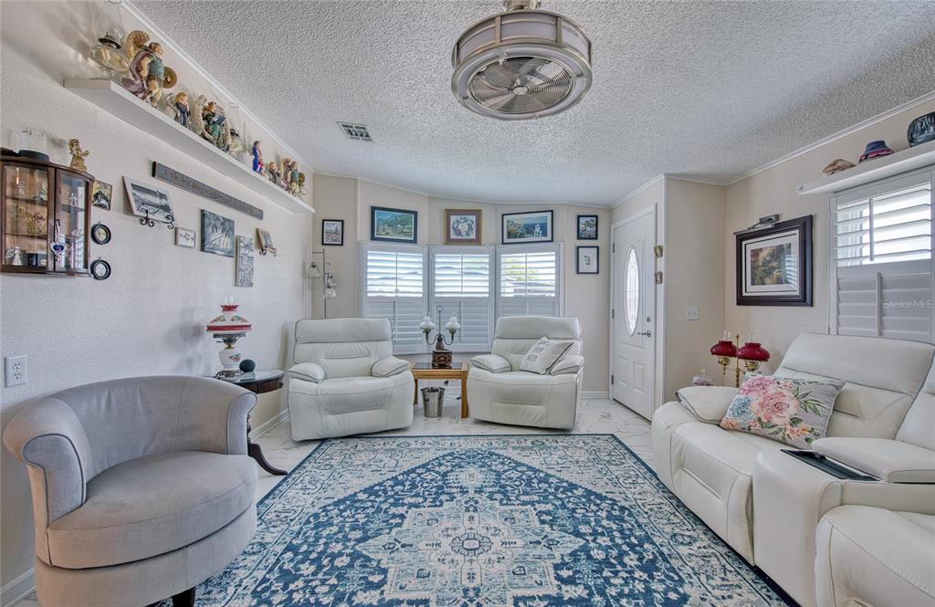 A living room features white leather furniture, a blue patterned rug, and a ceiling fan — 214 DOLPHIN DRIVE N, OLDSMAR, FL