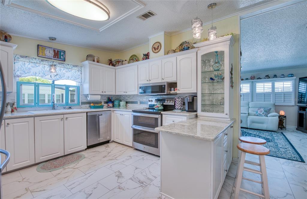 A kitchen features white cabinets, stainless steel appliances, granite countertops, and white marble-patterned tile flooring — 214 DOLPHIN DRIVE N, OLDSMAR, FL