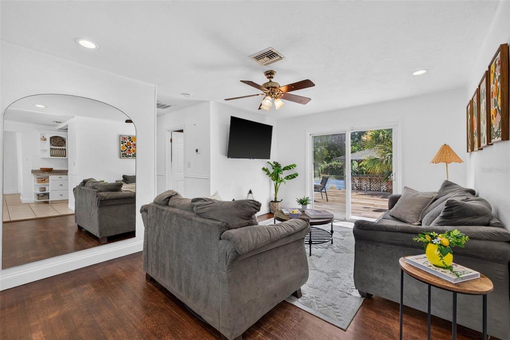 A living room features two gray sofas, a large arched mirror, and sliding glass doors — 166 PINELLAS WAY N, ST PETERSBURG, FL