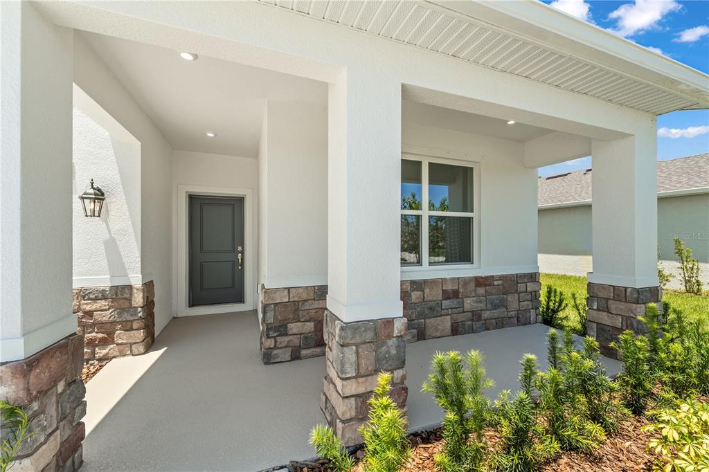 A covered front porch features white columns, stone veneer accents, and a dark gray door — 10165 HUNTINGNET WAY, LEESBURG, FL