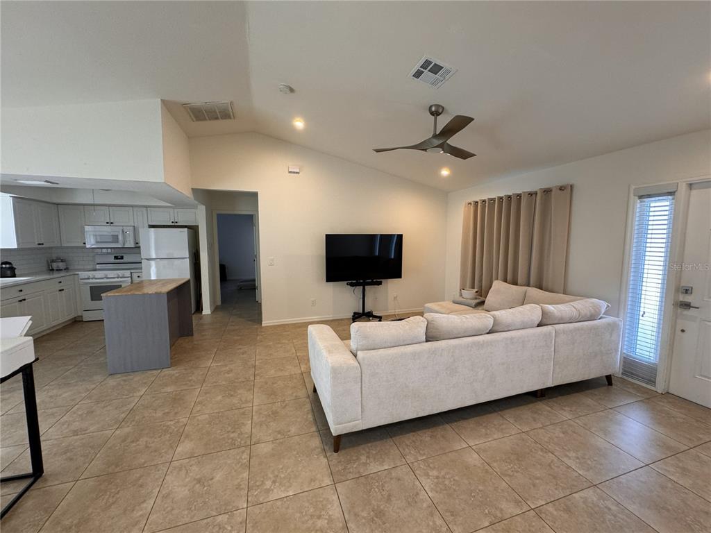A living room with tile floors, a sectional sofa, and a television faces an open kitchen — 3806 SW 6TH AVENUE, CAPE CORAL, FL