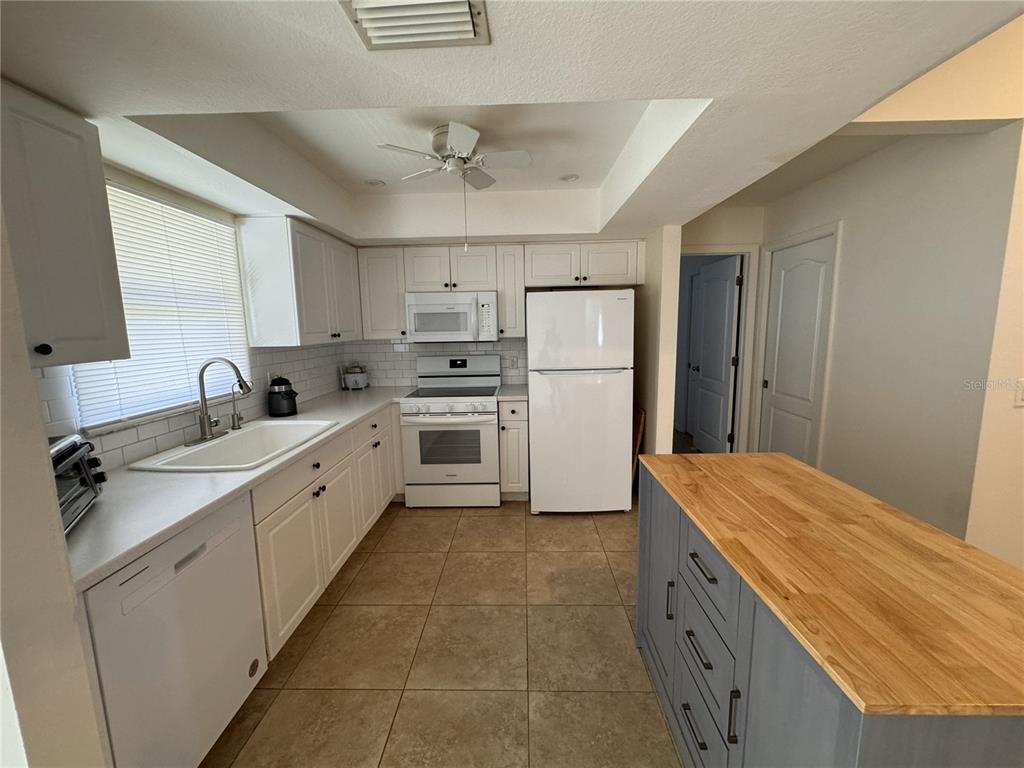 A kitchen features white cabinetry, white appliances, tile flooring, and a gray island with wood countertop — 3806 SW 6TH AVENUE, CAPE CORAL, FL