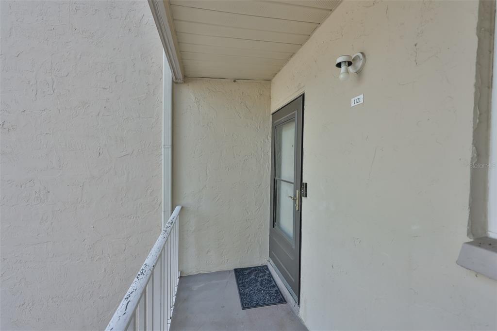 An exterior view of a covered apartment entryway with a door numbered 1121 — 2625 STATE ROAD 590 UNIT 1121, CLEARWATER, FL