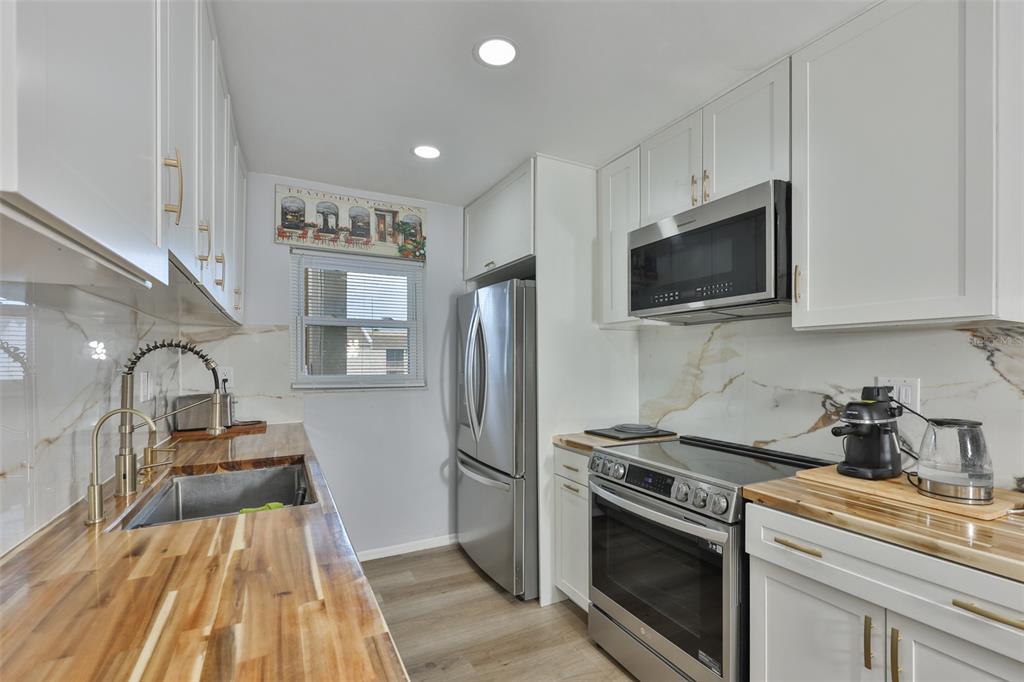A kitchen features white cabinets, stainless steel appliances, and wood countertops with marble-style backsplashes — 2625 STATE ROAD 590 UNIT 1121, CLEARWATER, FL