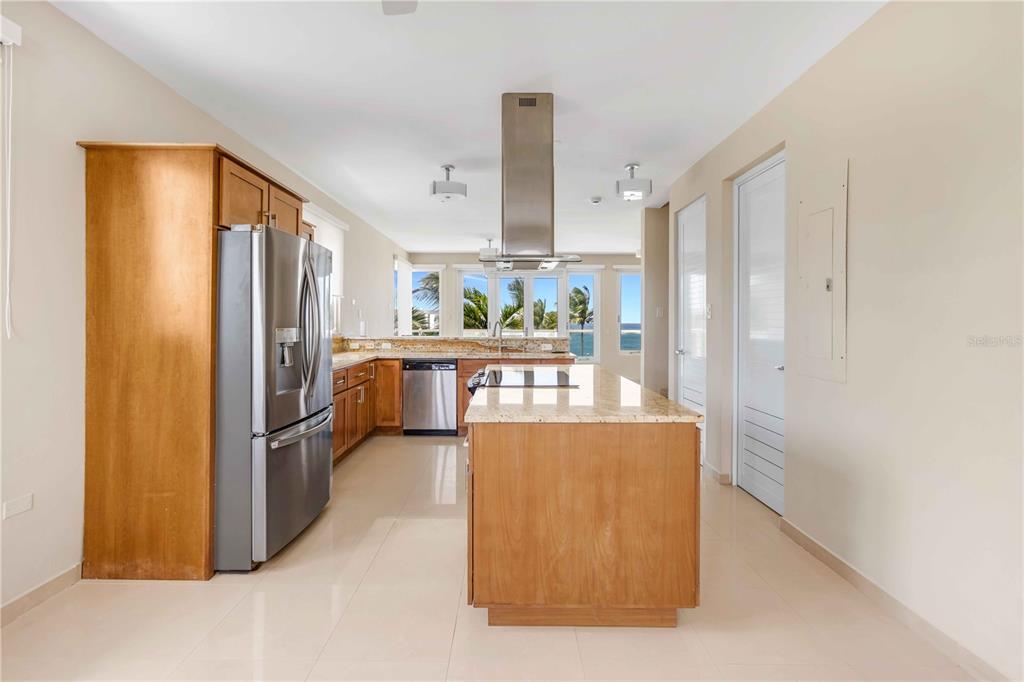 A kitchen features wood cabinets, stainless steel appliances, a granite island, and a view of the ocean — 7 PASEO DE LA BALANDRAS UNIT 7, DORADO, PR