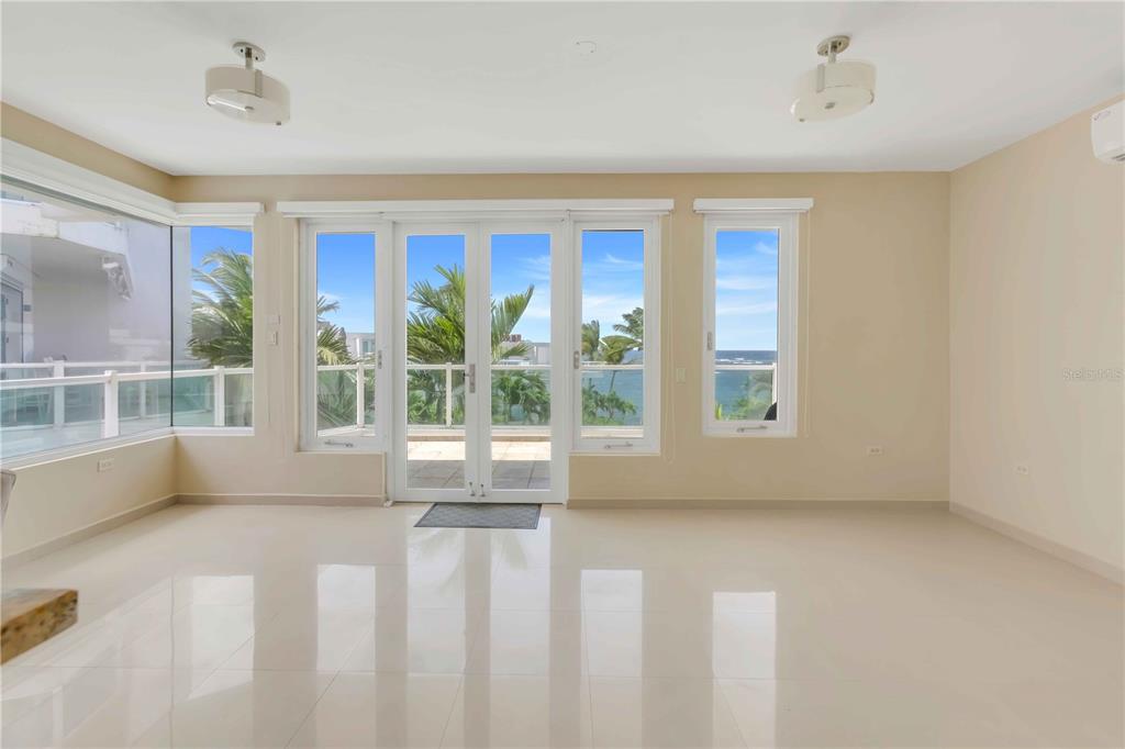 A bright, empty room with light tile floors, beige walls, and glass doors overlooking the ocean — 7 PASEO DE LA BALANDRAS UNIT 7, DORADO, PR