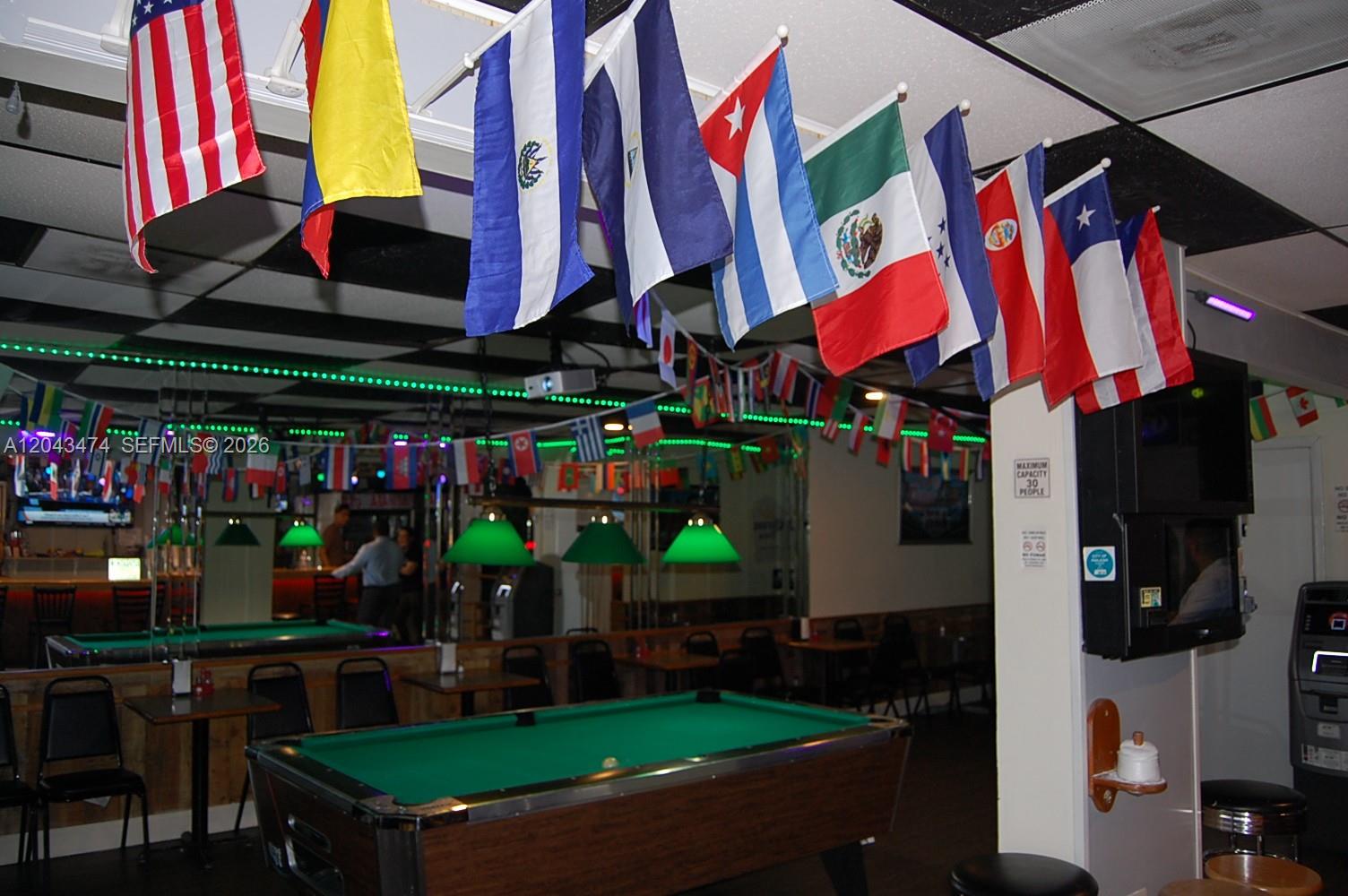 A pool hall features a billiard table, green pendant lighting, and international flags hanging from the ceiling — 883 W 29, Hialeah FL 33012, HIALEAH, FL
