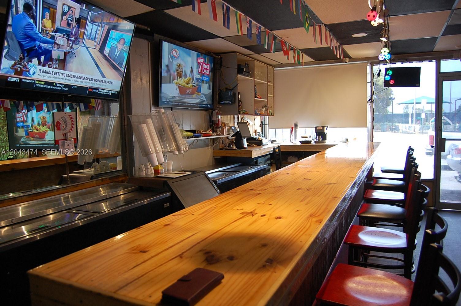 A long wooden bar counter with stools faces a service area with televisions and windows — 883 W 29, Hialeah FL 33012, HIALEAH, FL