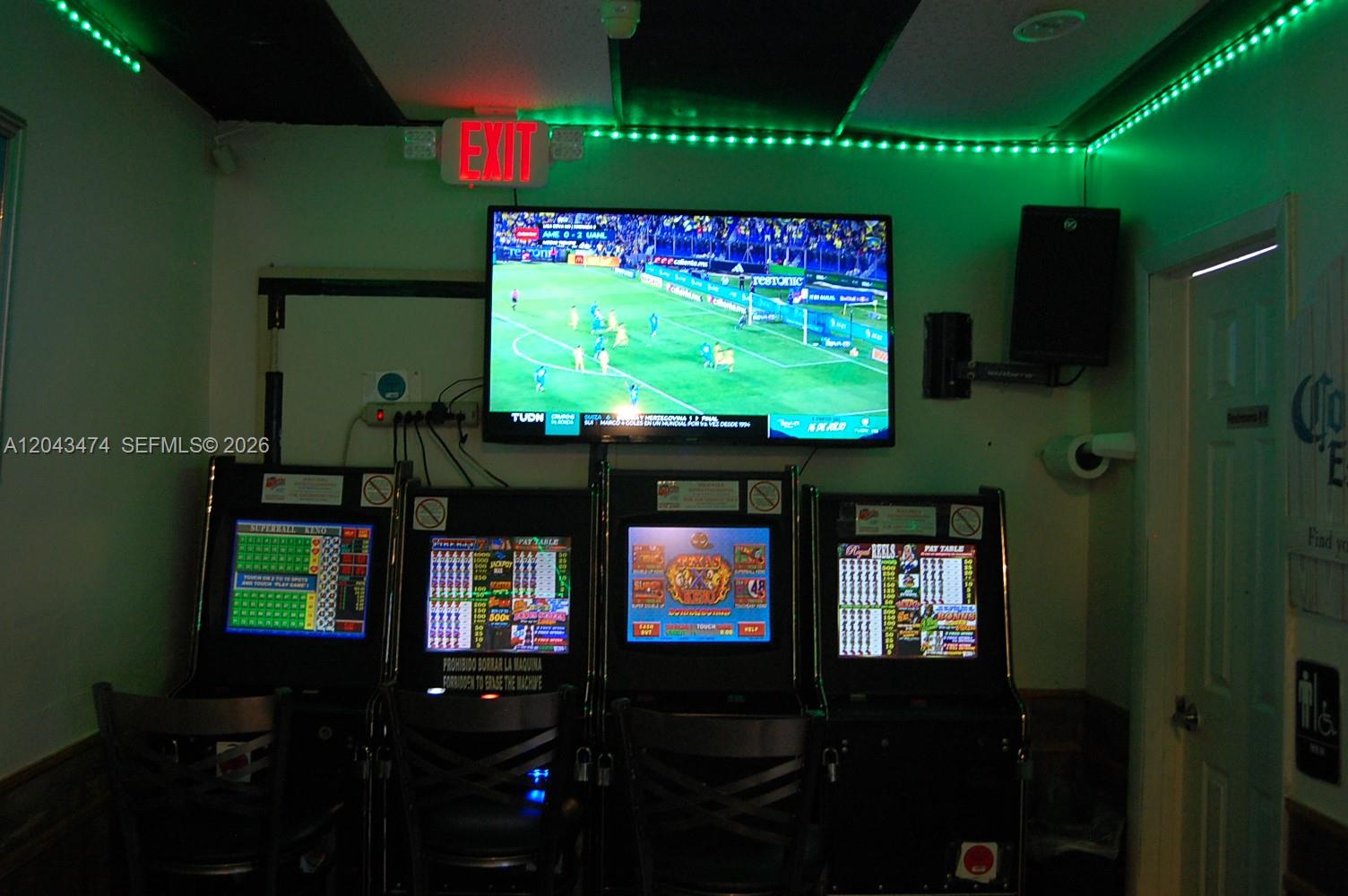 A room features four gaming machines positioned beneath a wall-mounted television displaying a soccer match — 883 W 29, Hialeah FL 33012, HIALEAH, FL