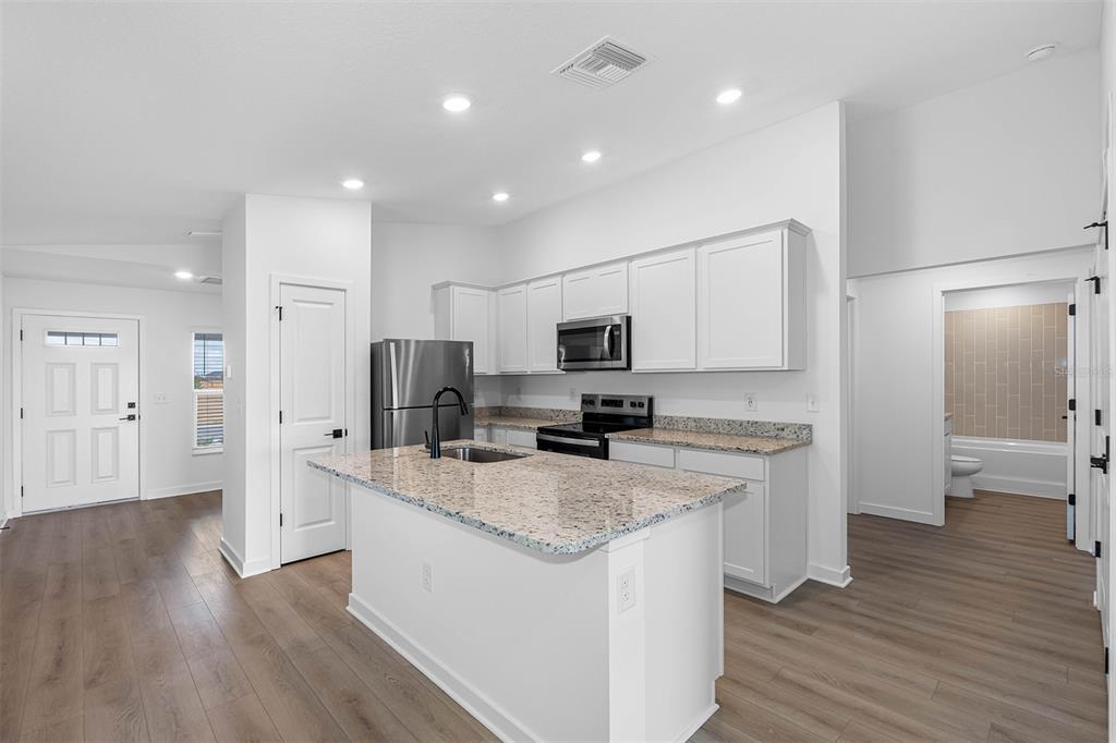 A kitchen features white cabinets, granite countertops, a center island, and wood-look flooring — 29677 FEDORA CIRCLE, BROOKSVILLE, FL