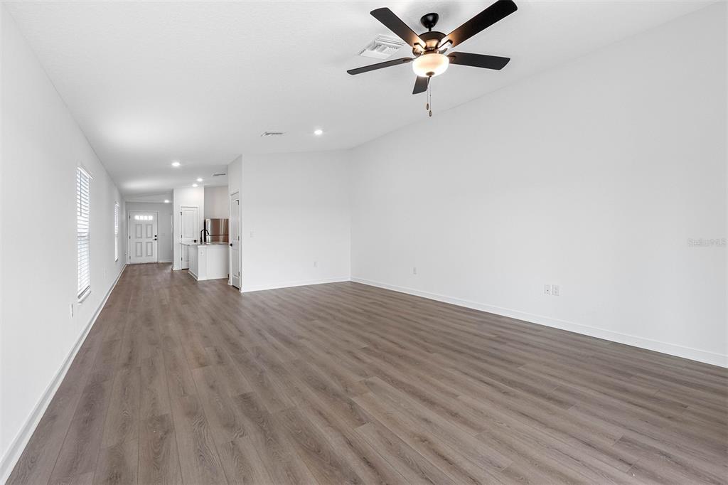 A spacious, empty living room with wood-look flooring, white walls, and a ceiling fan — 29677 FEDORA CIRCLE, BROOKSVILLE, FL