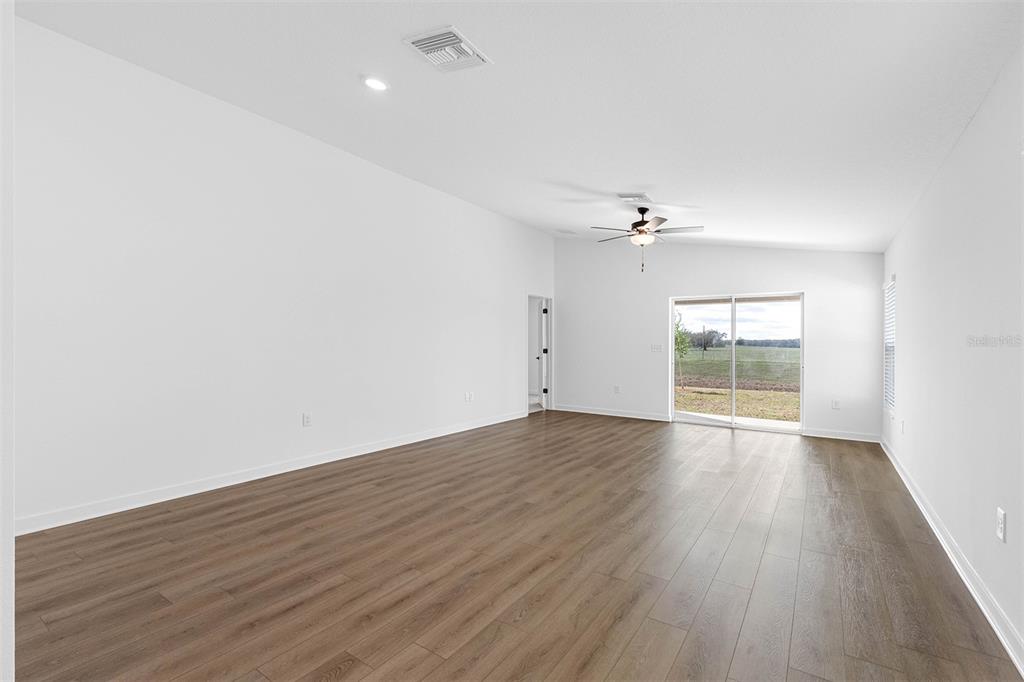 An empty living room with wood-look flooring, a ceiling fan, and sliding glass doors — 29677 FEDORA CIRCLE, BROOKSVILLE, FL