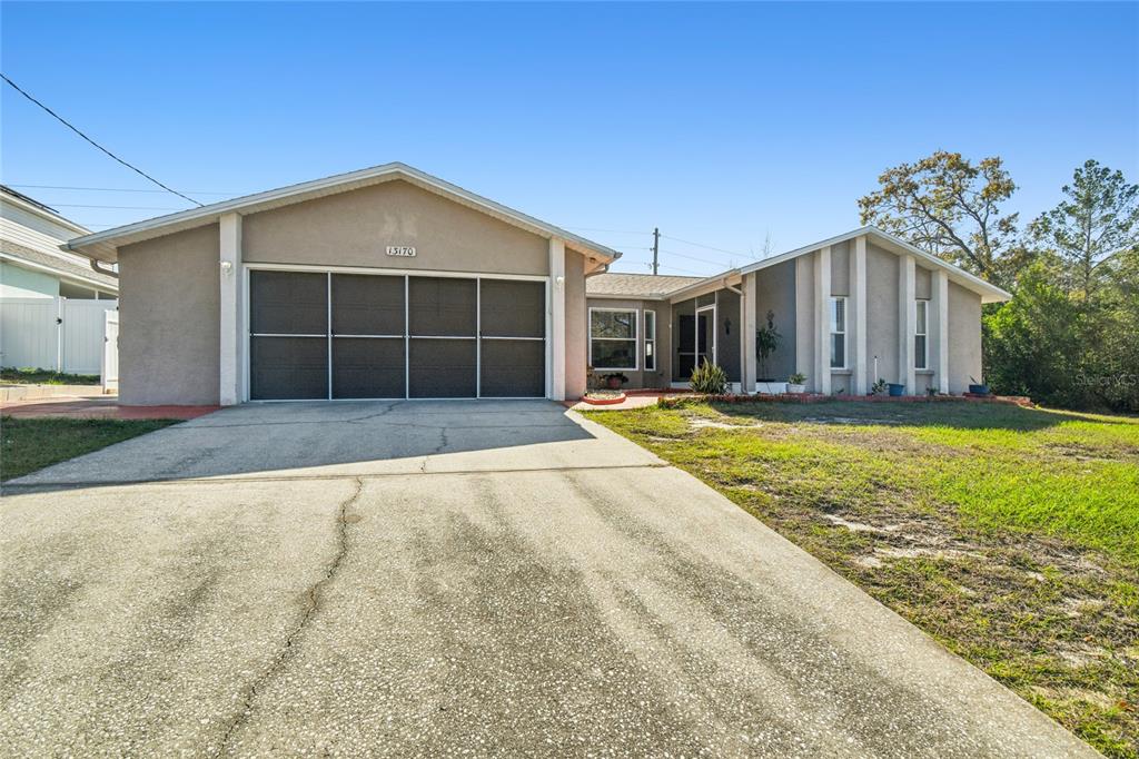 A single-story house with a beige stucco exterior, a large garage, and a concrete driveway — 13170 PIRATE LANE, SPRING HILL, FL
