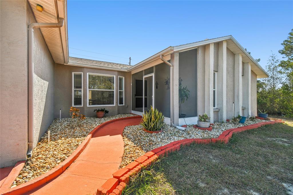 A red concrete walkway leads to the screened-in entryway of a stucco house — 13170 PIRATE LANE, SPRING HILL, FL