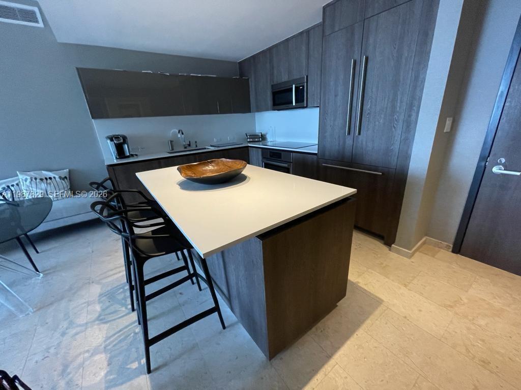 A modern kitchen features dark wood cabinetry, a white island countertop, and light tile flooring — 88 SW 7th St # 3609, Miami FL 33130, MIAMI, FL