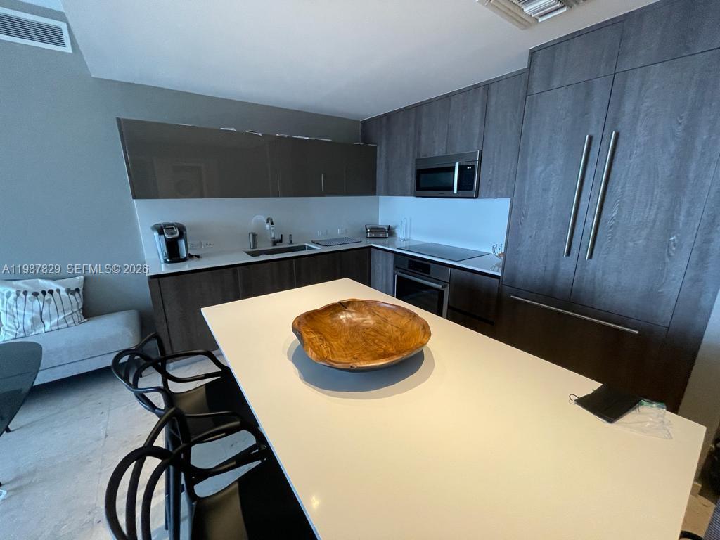 A modern kitchen features dark wood cabinetry, a white island, and stainless steel appliances — 88 SW 7th St # 3609, Miami FL 33130, MIAMI, FL