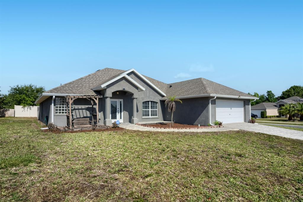 A single-story gray stucco house with a two-car garage and a front porch swing — 4460 MARSH HARBOR DRIVE, TAVARES, FL