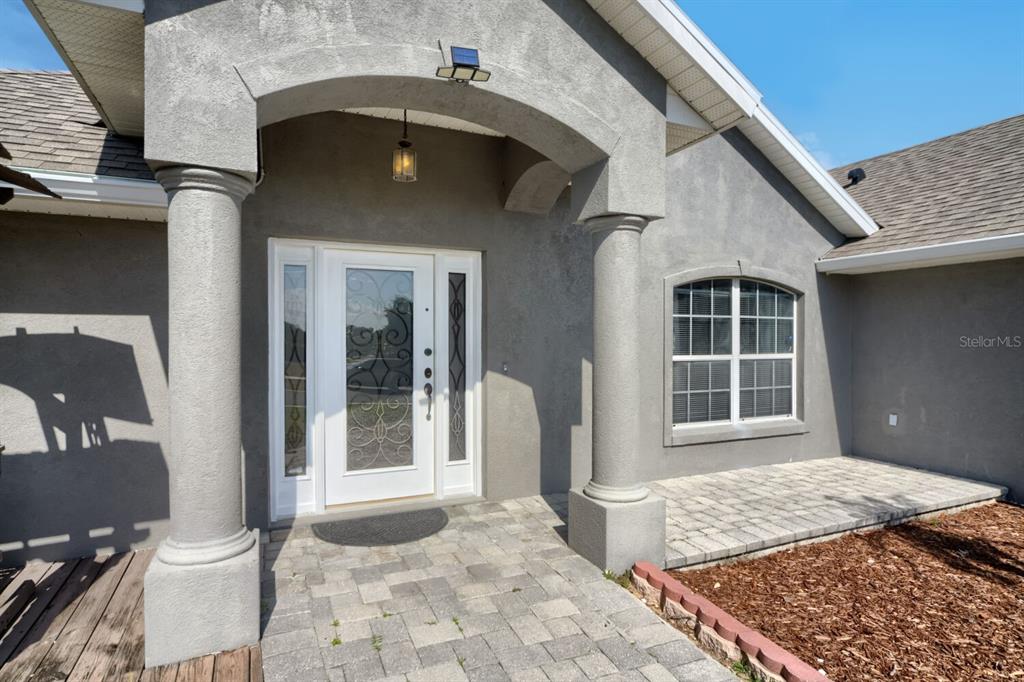 A gray stucco house exterior features a covered entryway with columns and a glass door — 4460 MARSH HARBOR DRIVE, TAVARES, FL