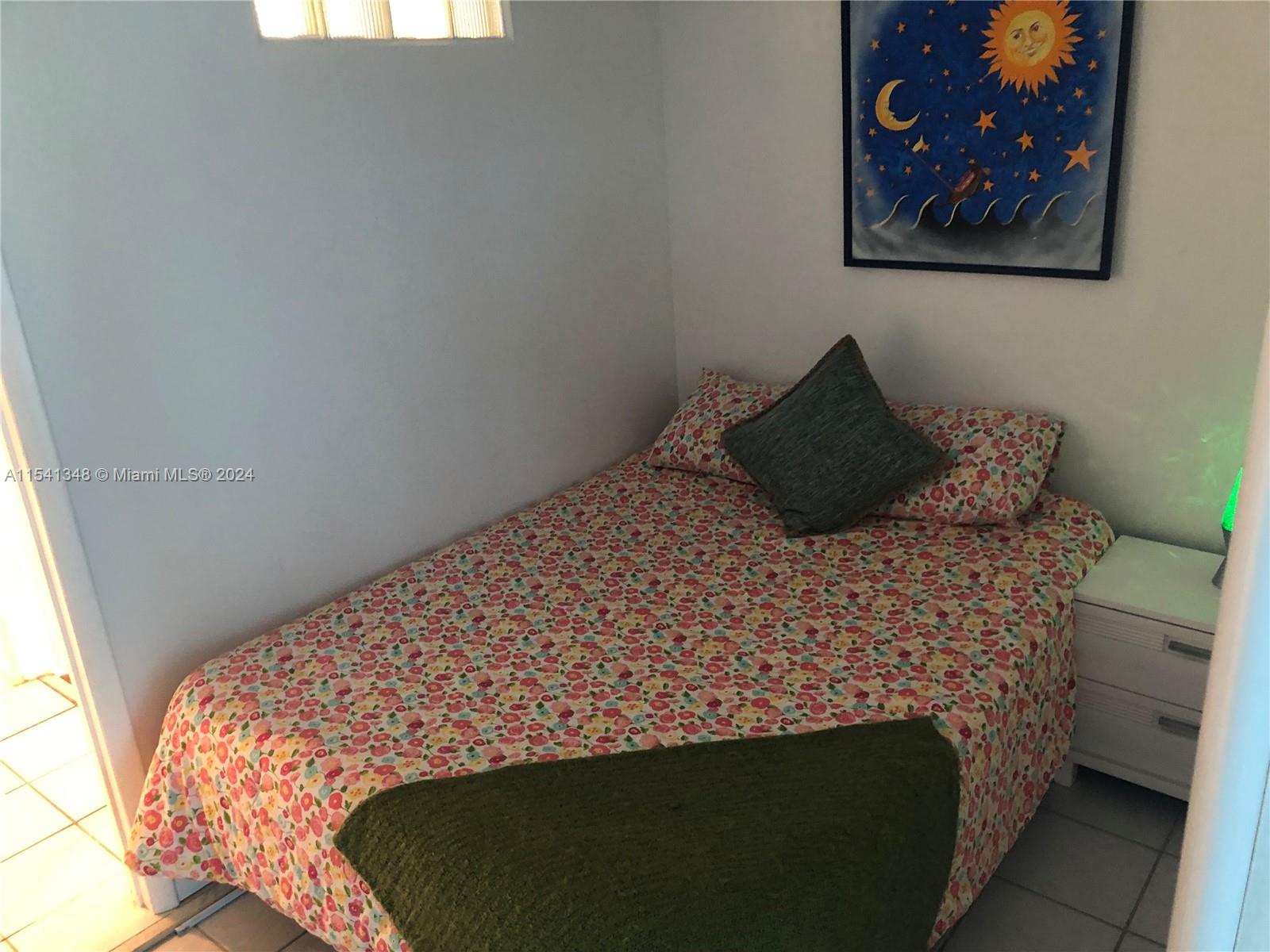 A bedroom features a floral bedspread, a dark accent pillow, and a sun-themed wall painting — 5445 Collins Ave, Miami Beach FL 33140, MIAMI BEACH, FL