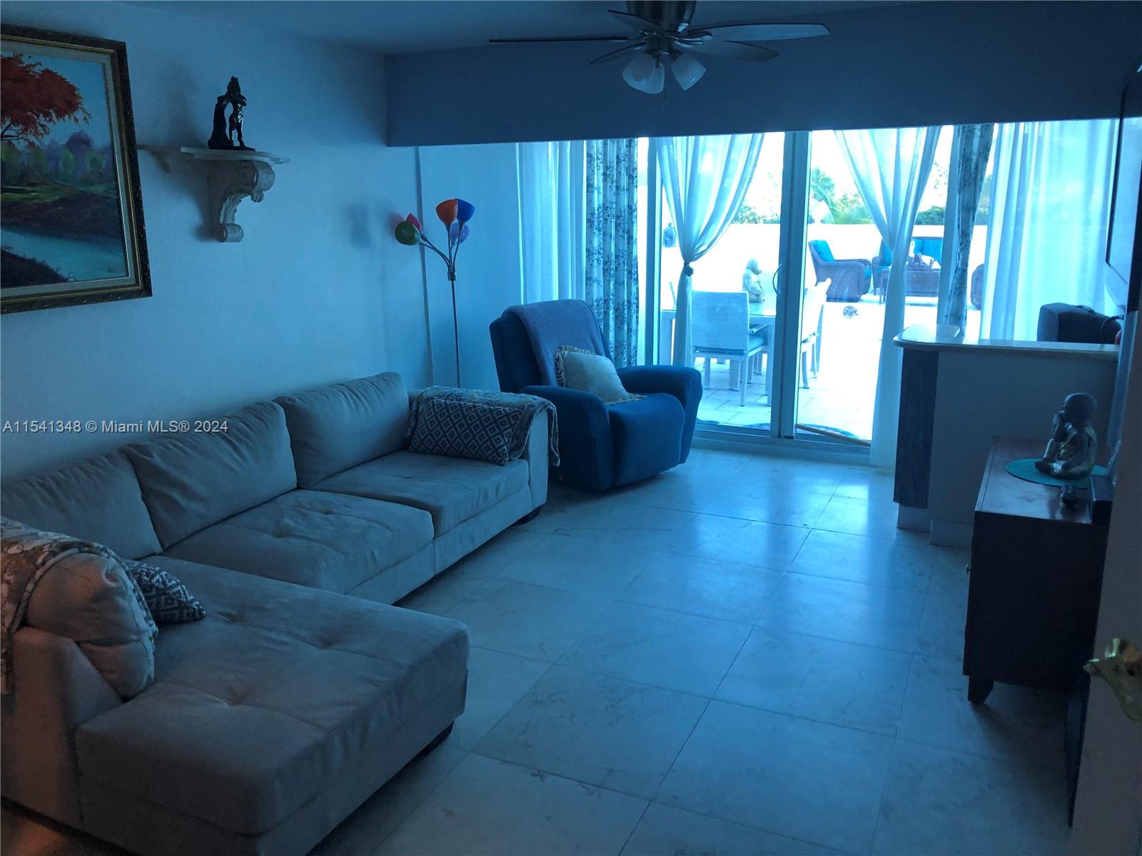 A living room features a light-colored sectional sofa, a blue armchair, and sliding glass doors — 5445 Collins Ave, Miami Beach FL 33140, MIAMI BEACH, FL
