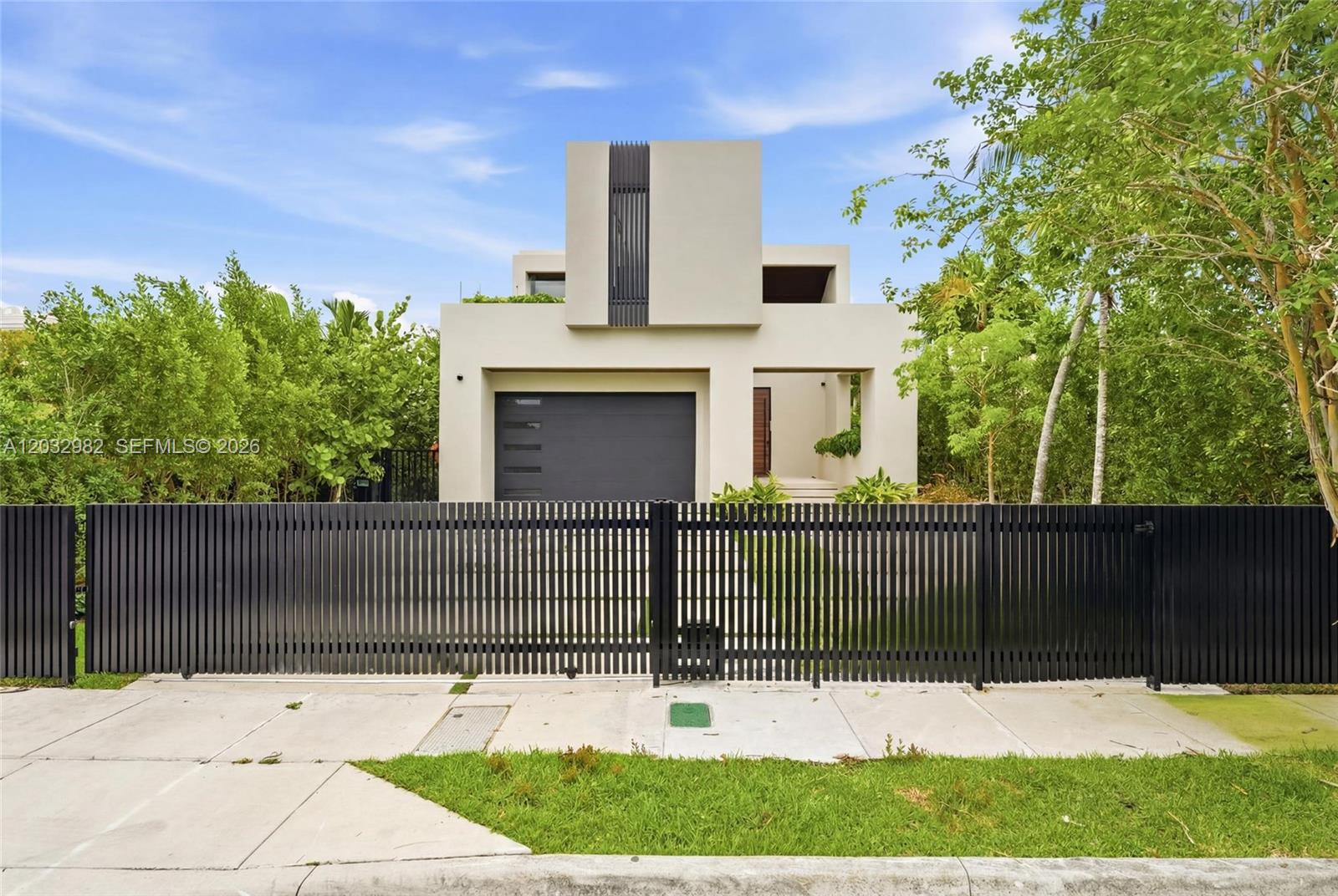 A modern two-story house with a black gate and garage door sits behind lush greenery — 1050 Stillwater Dr, Miami Beach FL 33141, MIAMI BEACH, FL