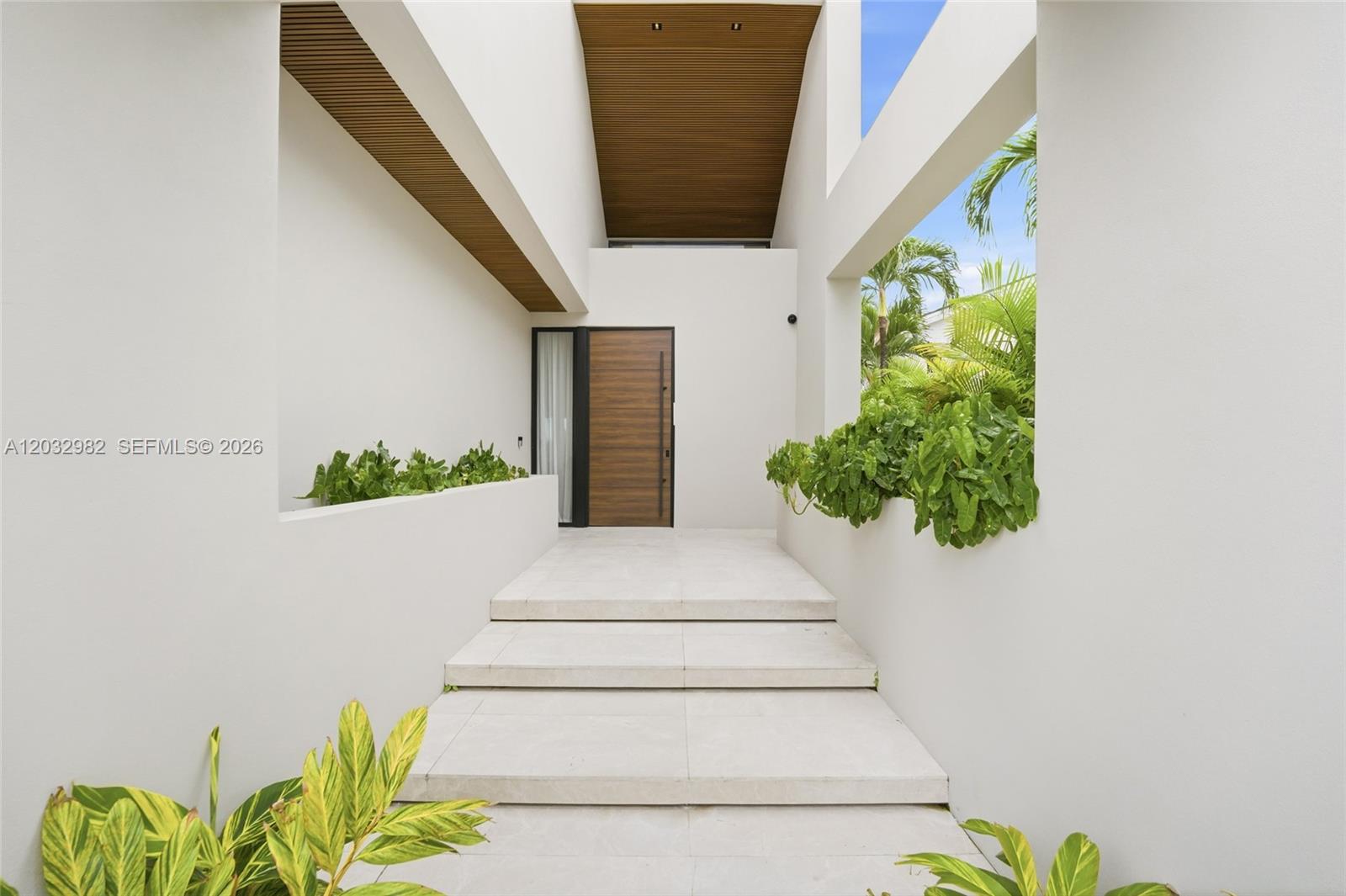 A modern entryway features white concrete steps leading to a wooden front door — 1050 Stillwater Dr, Miami Beach FL 33141, MIAMI BEACH, FL