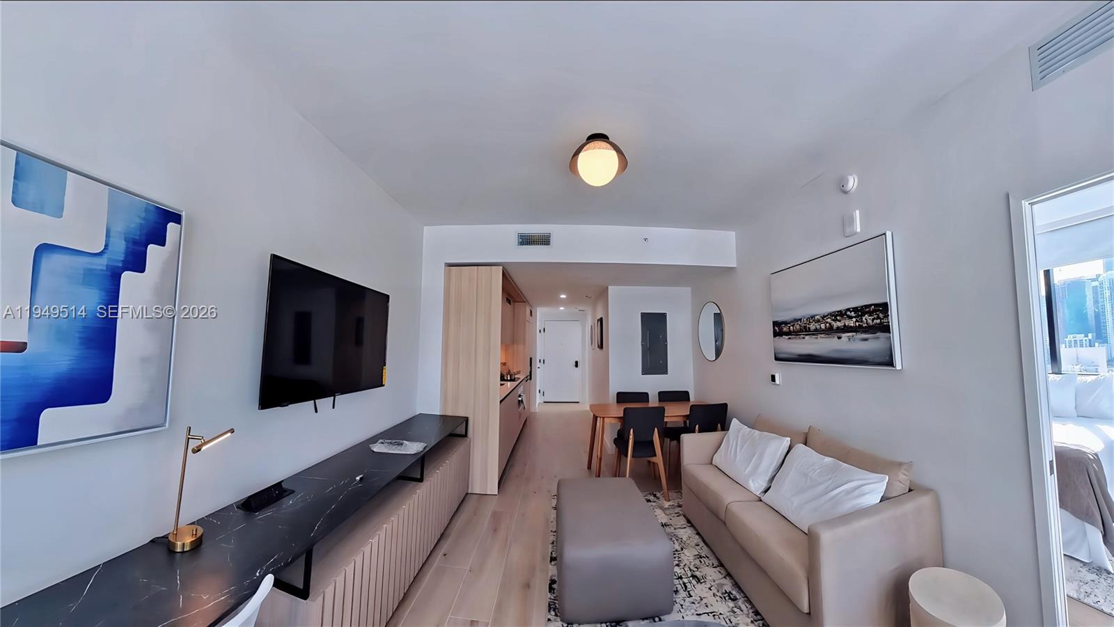 A modern living room features a sofa, television, dining area, and light wood flooring — 225 N Miami Ave # 1812, Miami FL 33132, MIAMI, FL