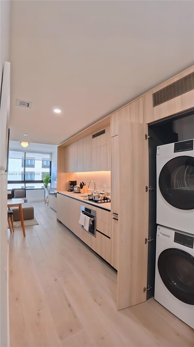A modern kitchen features light wood cabinetry, integrated appliances, and a stacked washer and dryer — 225 N Miami Ave # 1812, Miami FL 33132, MIAMI, FL