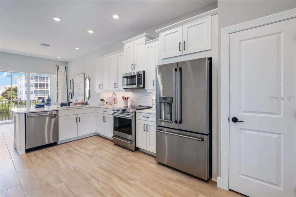 A modern kitchen features white cabinetry, stainless steel appliances, and light wood-look flooring — 1623 SEA HAVEN DRIVE UNIT 306, PUNTA GORDA, FL