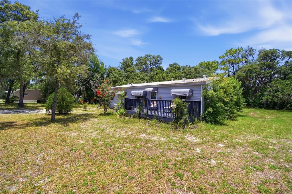 A single-story manufactured home with a dark wooden deck sits on a grassy lot — 6261 W MONTICELLO STREET, HOMOSASSA, FL