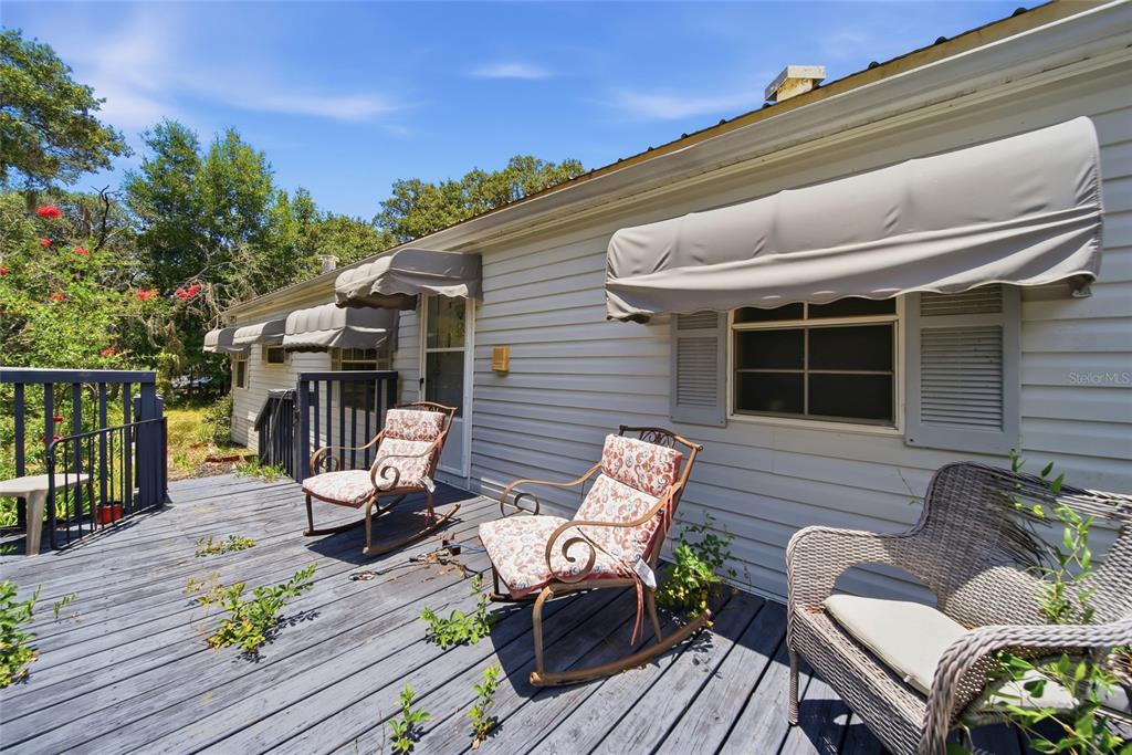 A wooden deck with three chairs sits outside a house with light-colored siding and awnings — 6261 W MONTICELLO STREET, HOMOSASSA, FL