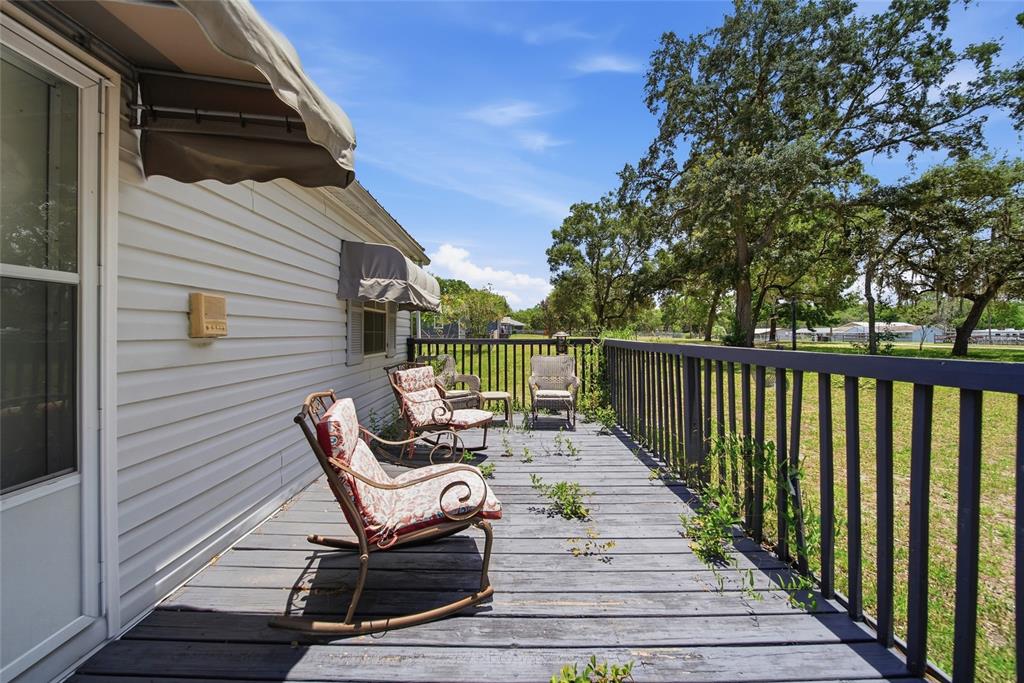 A wooden deck with rocking chairs and a railing overlooks a grassy yard with trees — 6261 W MONTICELLO STREET, HOMOSASSA, FL