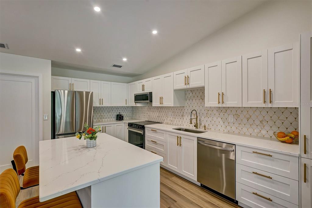 An open-concept living and dining area features wood-look flooring, modern furniture, and a white kitchen — 3925 OAKHURST BOULEVARD, SARASOTA, FL