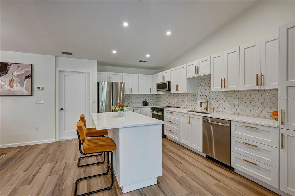 A modern kitchen features white cabinets, stainless steel appliances, a marble island, and gold hardware — 3925 OAKHURST BOULEVARD, SARASOTA, FL