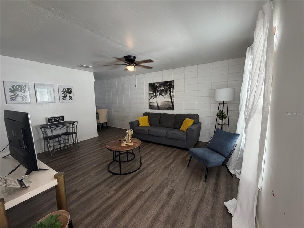 A living room features a gray sofa, a blue accent chair, and wood-look flooring — 15219 WESTMINISTER AVENUE UNIT B, CLEARWATER, FL