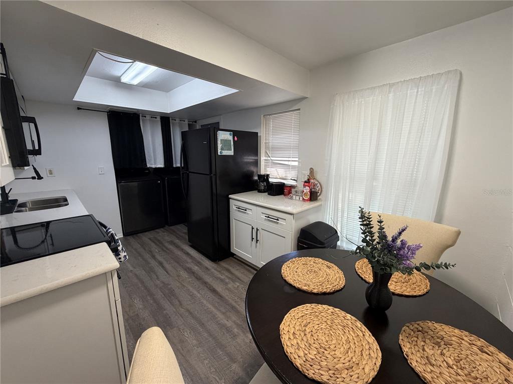 A kitchen features white cabinets, black appliances, a dining table, and wood-look flooring — 15219 WESTMINISTER AVENUE UNIT B, CLEARWATER, FL