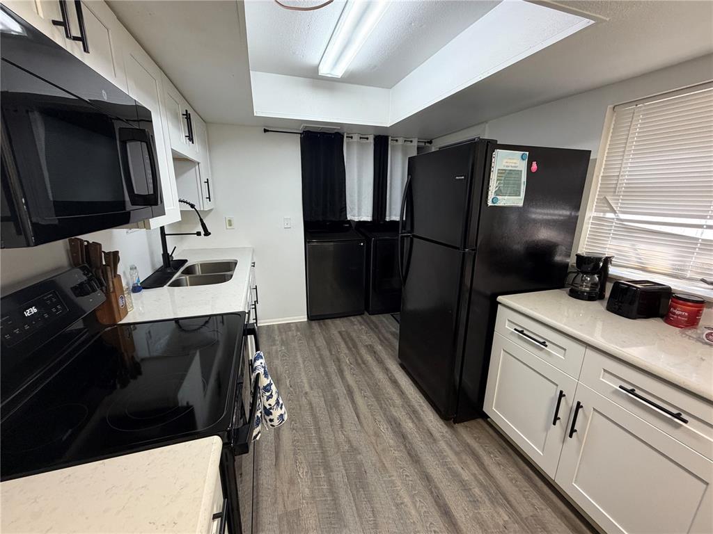 A kitchen features white cabinets, black appliances, light countertops, and wood-look flooring — 15219 WESTMINISTER AVENUE UNIT B, CLEARWATER, FL