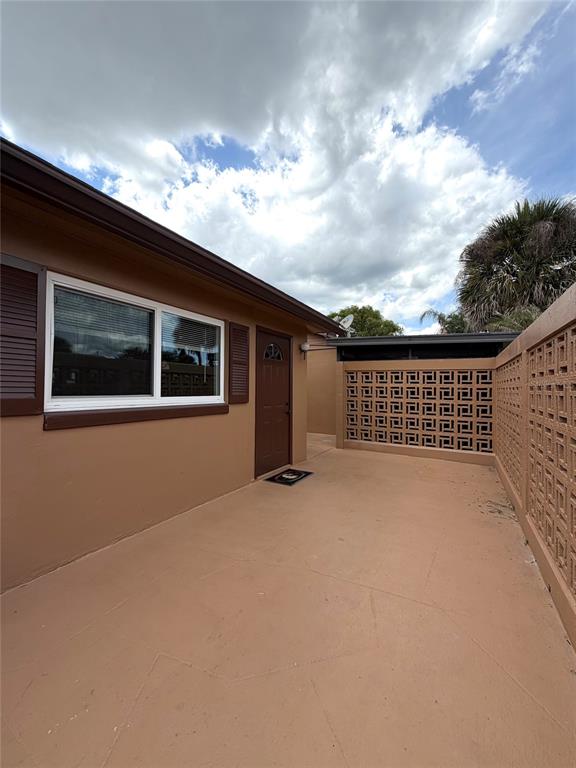 A tan exterior wall with a window and door faces a concrete patio enclosed by breeze blocks — 432 E STREET UNIT 432, CASSELBERRY, FL