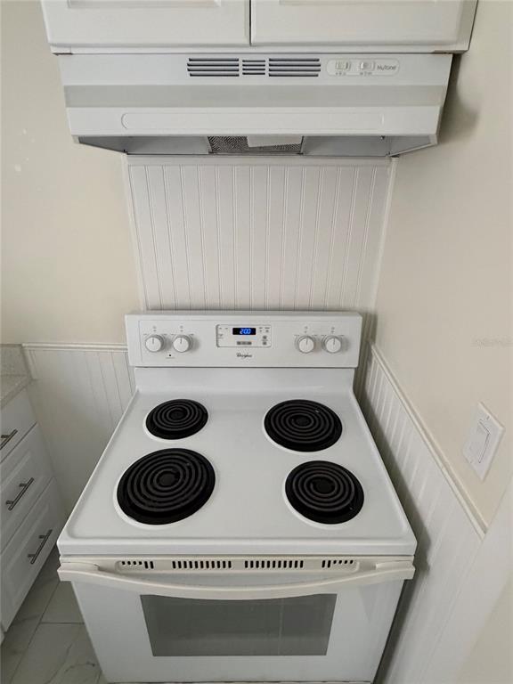 A white electric stove sits beneath a range hood in a kitchen with beadboard walls — 432 E STREET UNIT 432, CASSELBERRY, FL