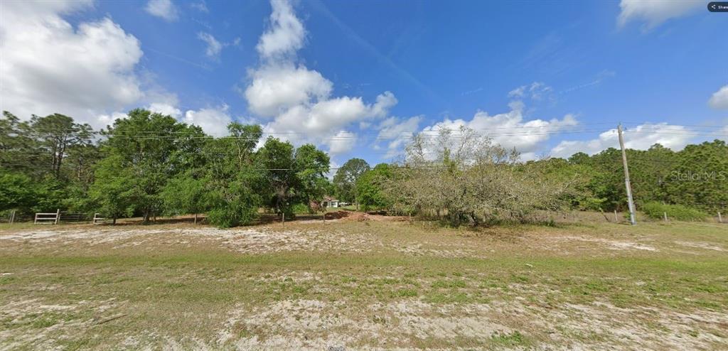 A wide, grassy, and sandy vacant lot features scattered trees and a distant house — COMMONWEALTH AVE N, POLK CITY, FL