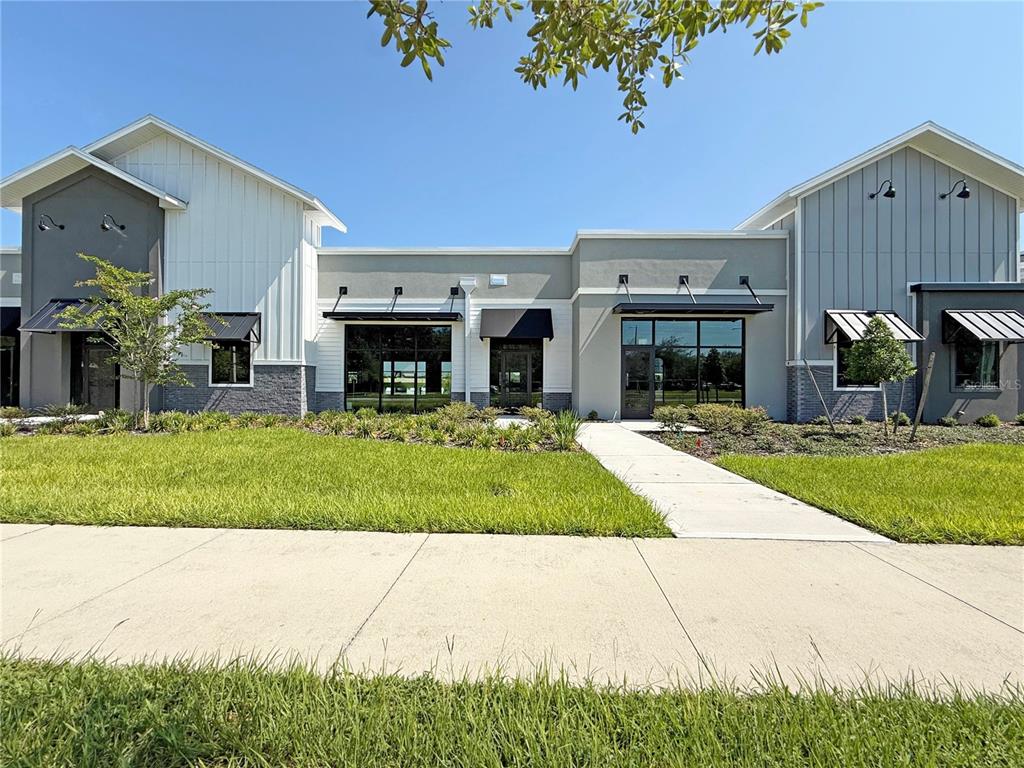 A modern commercial building exterior with gray and white siding, black awnings, and glass doors — 12143 STONEYBROOK WEST PARKWAY UNIT 101-102, WINTER GARDEN, FL