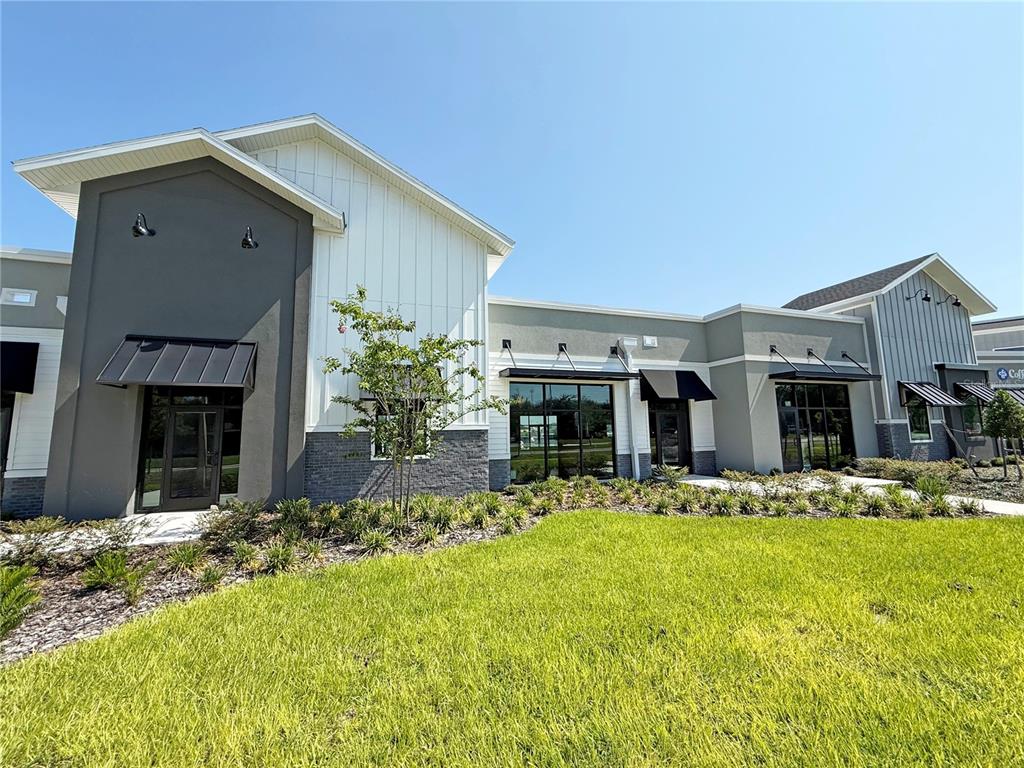 A modern commercial building exterior features white vertical siding, gray accents, and dark metal awnings — 12143 STONEYBROOK WEST PARKWAY UNIT 101-102, WINTER GARDEN, FL