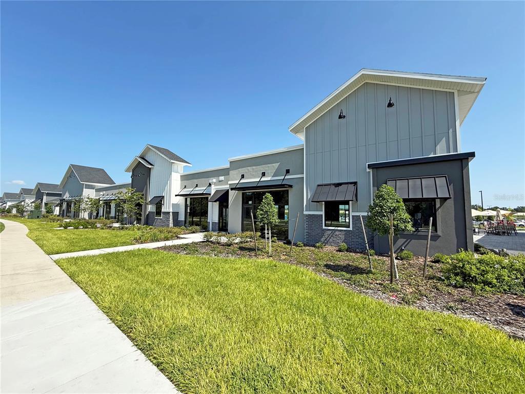 A modern commercial building with gray siding and brick accents sits beside a concrete sidewalk — 12143 STONEYBROOK WEST PARKWAY UNIT 101-102, WINTER GARDEN, FL