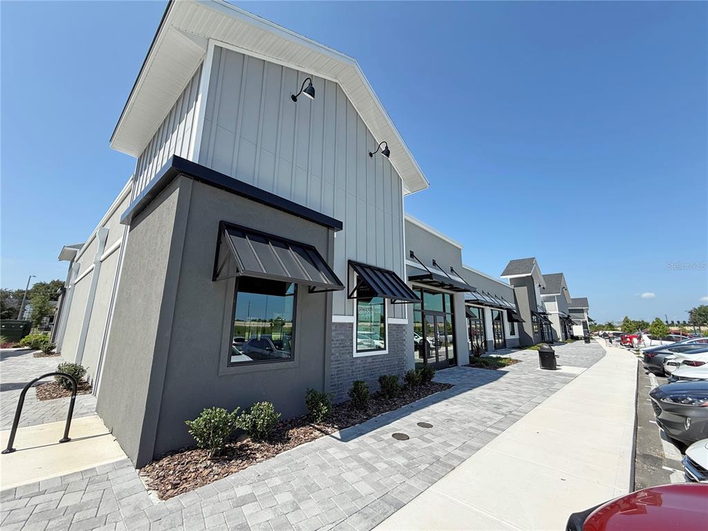 A modern commercial building exterior features gray vertical siding, dark metal awnings, and brick accents — 12143 STONEYBROOK WEST PARKWAY UNIT 101-102, WINTER GARDEN, FL