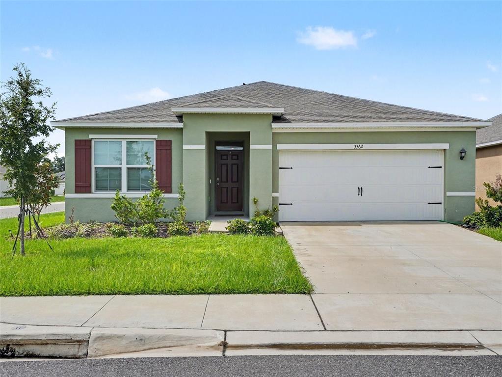A single-story house with green stucco siding, a two-car garage, and a dark front door — 3362 ARUBA WAY, HAINES CITY, FL