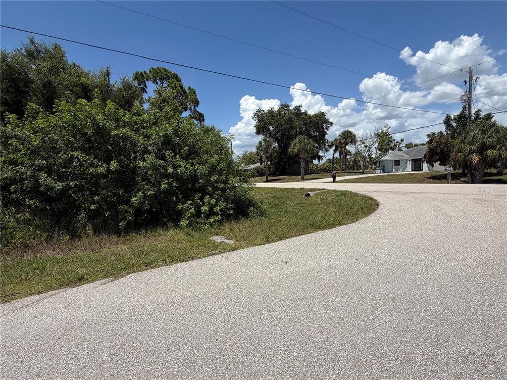 A paved road curves past a grassy lot with dense bushes and distant houses — 17224 CLIFF AVENUE, PORT CHARLOTTE, FL