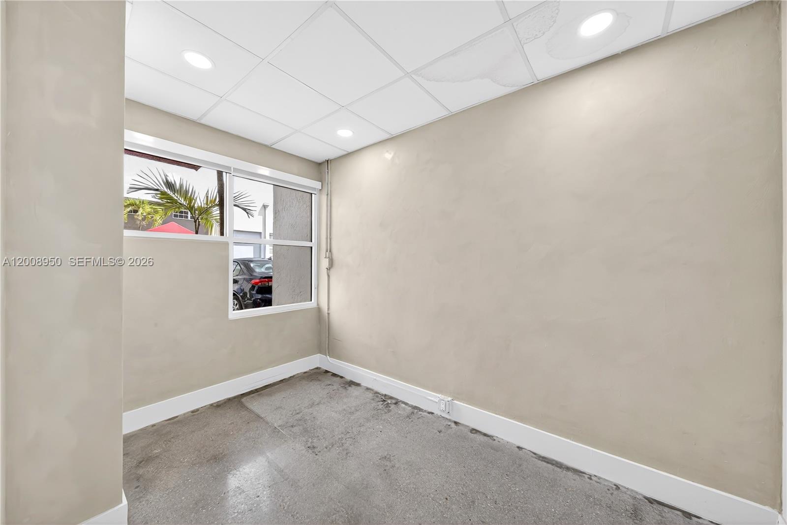 A small, empty room features beige walls, a drop ceiling, and a concrete floor — 12305 SW 133rd Ct # 26, Miami FL 33186, MIAMI, FL