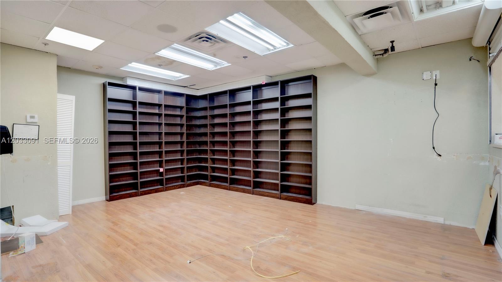 An empty room features wood-look flooring, light green walls, and built-in dark wood shelving units — 304 SW 12 Ave, Miami FL 33130, MIAMI, FL