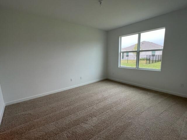 An empty bedroom features beige carpeting, white walls, and a window overlooking a fenced yard — 2751 NE Breezeway Circle, Jensen Beach FL 34957, JENSEN BEACH, FL