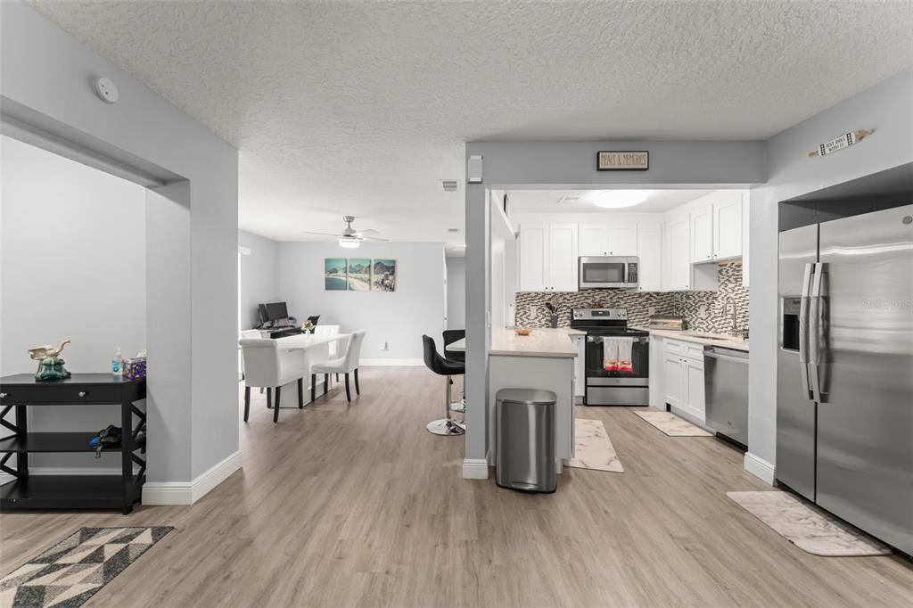 A kitchen with white cabinets and stainless steel appliances opens into a dining area — 1518 DAROCA DRIVE, DELTONA, FL